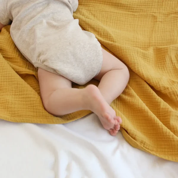bebé estirado bocabajo encima muselina color mostaza